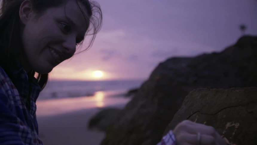 A woman smiles and writes initials on a rock