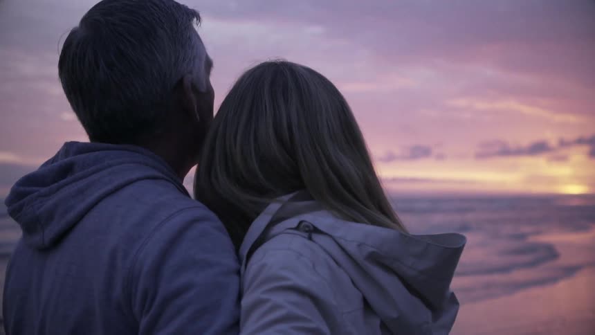 A man and woman embrace on a beach at sunset