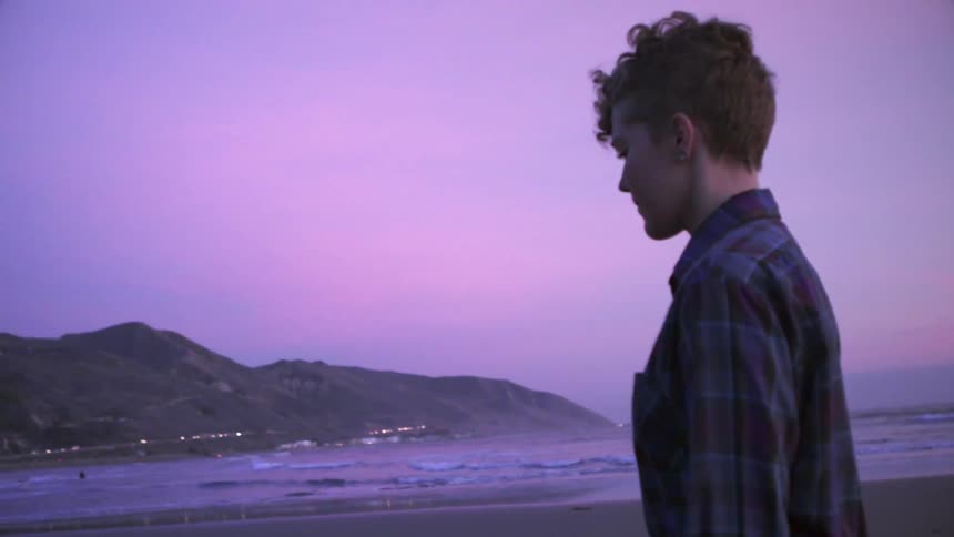 A woman is walking along the beach at sunset