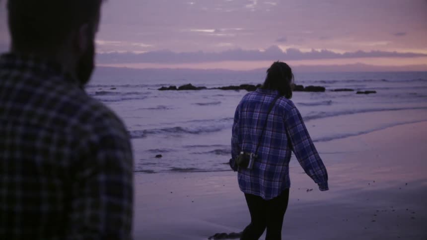 A man and women walk along the beach at sunset