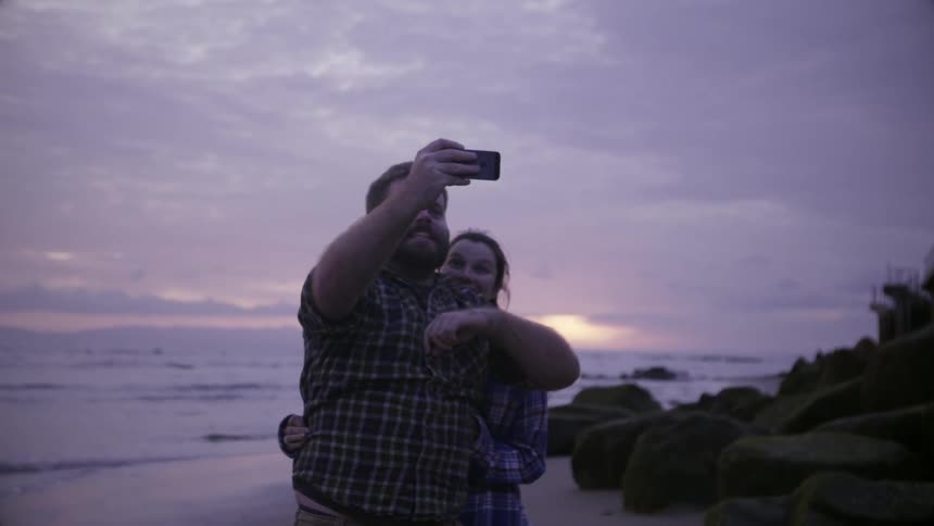 A man takes a photo with a woman on the beach