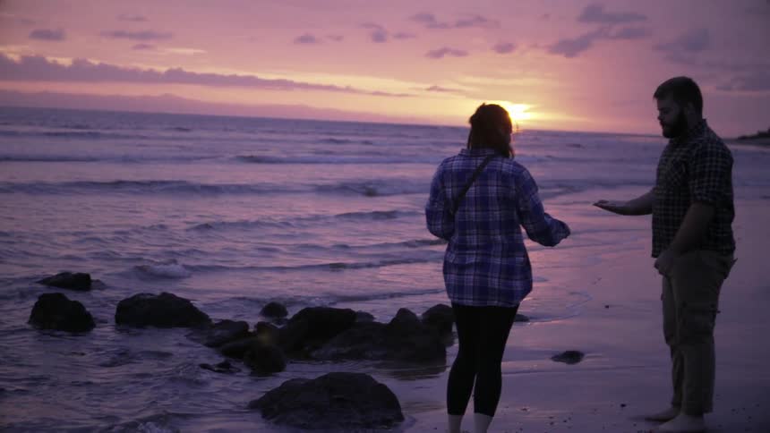 A woman picks something up and hands it to a man on the beach