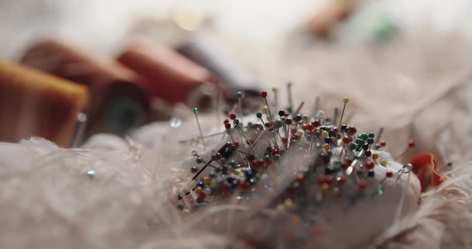 Person removes and replaces pins into a pincushion sitting on white fabric