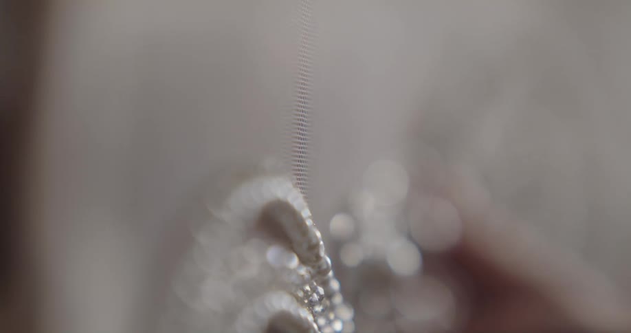 A seamstress sewing beads and pearls onto white fabric