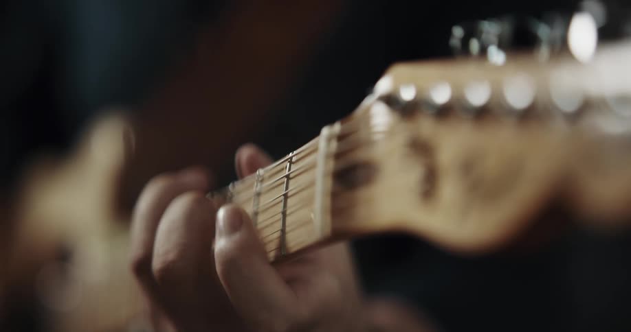 A person positions their fingers on the neck of a guitar while playing it