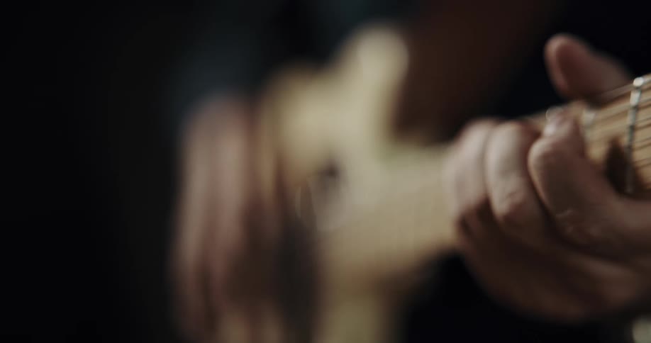 A person positions their fingers on the neck of a guitar while playing chords on it