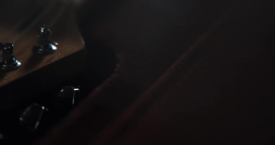 Close up of a person picking up an acoustic guitar from a case inside a dimly lit room