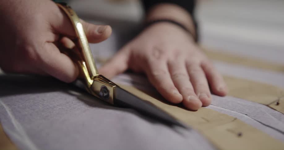 Tailor with black sweatshirt cuts cloth with golden scissor in tailor shop