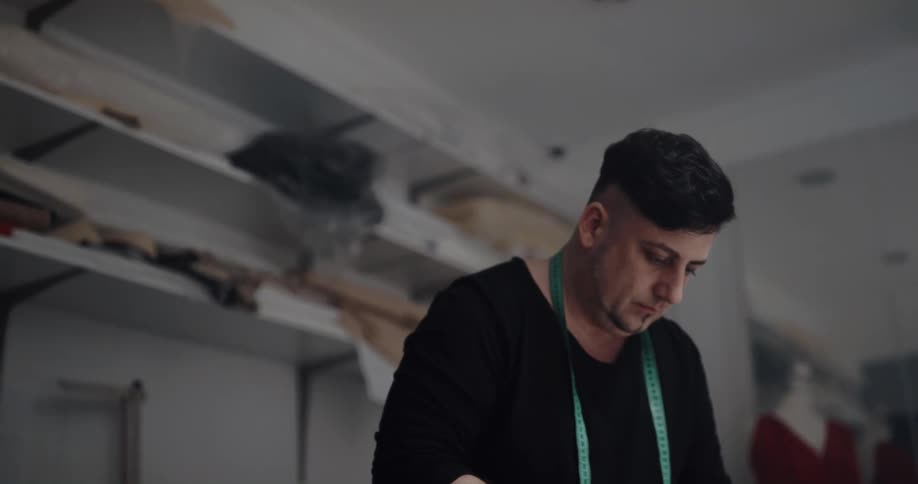 A man is standing with a tape measure around his neck and he pick up scissors and cuts something