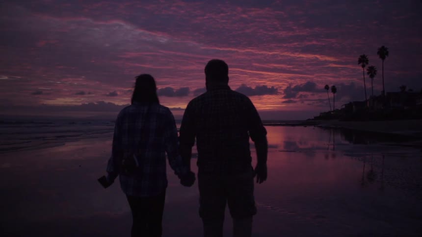 A couple walks on a beach at sunset