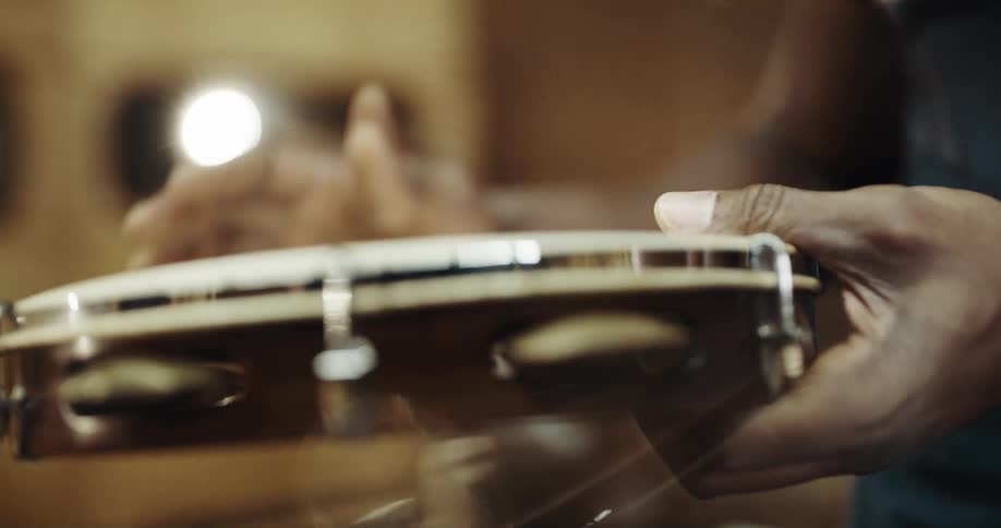 Musician turns and taps a tambourine while tunning it inside a room