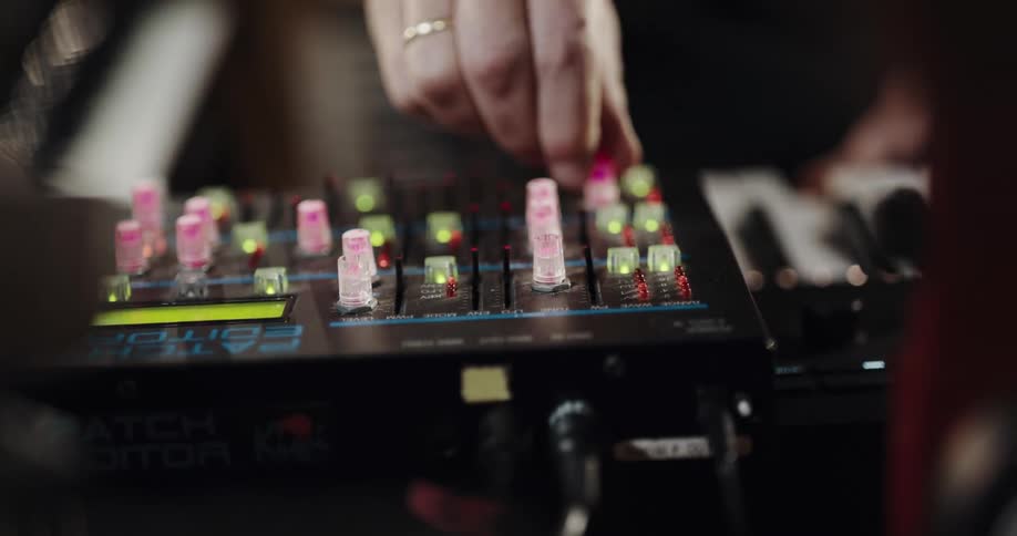 Man turning the colorful led lit knobs of an electronic device attached to a music keyboard