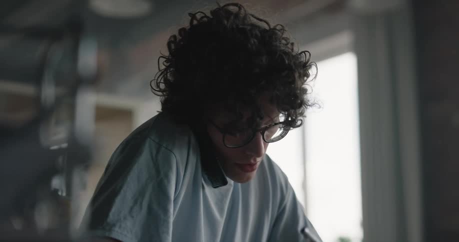 Teenage boy sitting at the desk studying on his notebook and laptop while talking to the phone