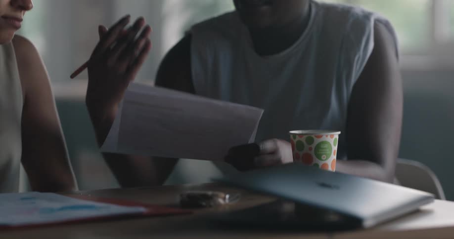Two women sitting on the table at an office space with a woman helping another with some papers