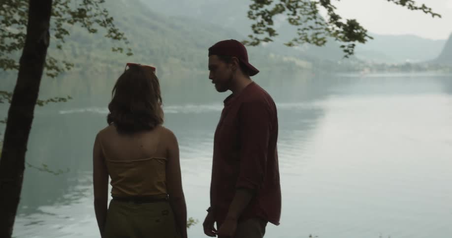 Upset woman standing near a lake when her boyfriend approaches and tries to apologize for something by gently touching her but she dodges him