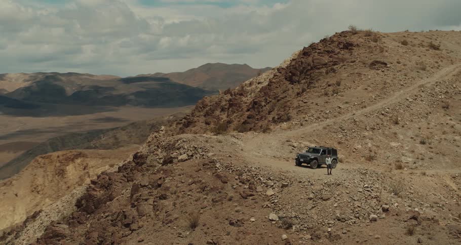 A jeep is parked on a dirt road in the mountains and a man is walking around