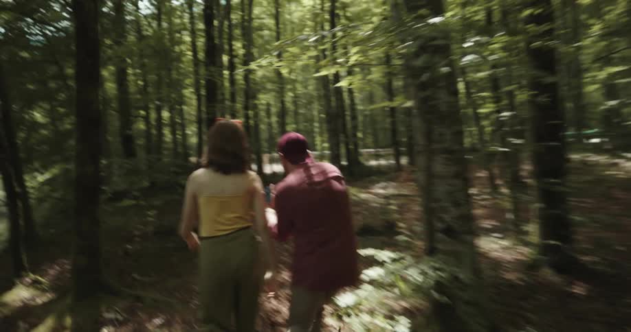 A man and woman argue about a smartphone while walking through a woodland during the day