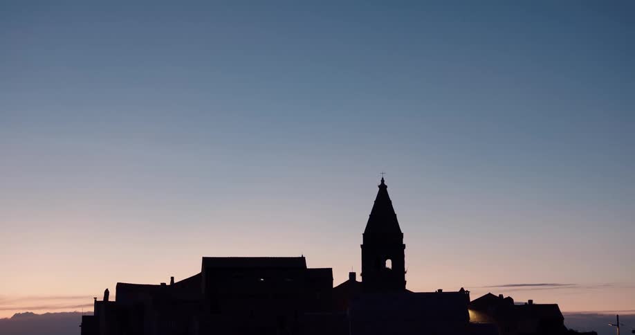 Silhouette of church with steeple and mountains in the background at sunset
