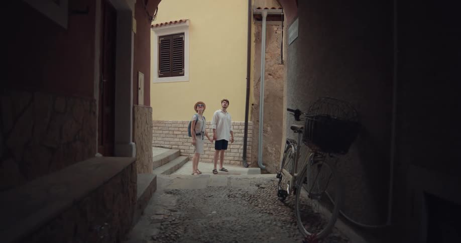 Alley of a tourist city with a bike parked on the wall with a couple holding hands passing by at the background
