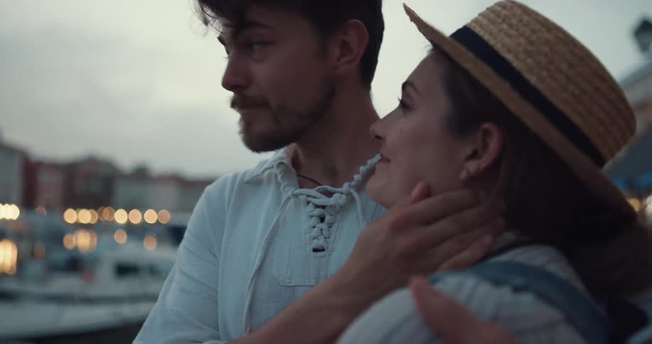 A couple embrace while standing along a river bank looking at a city