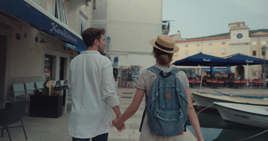 Tourist couple holding hands and walking through a tourist city in the border of a lake