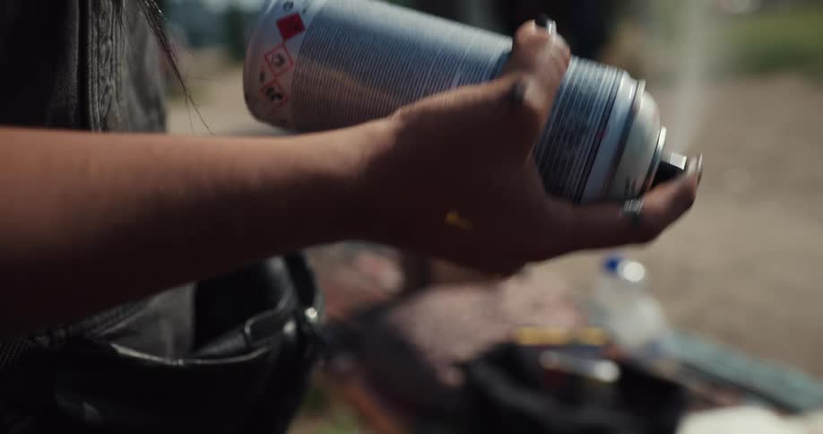 Someone shakes a white spray can then pushes the nozzle to spray the contents
