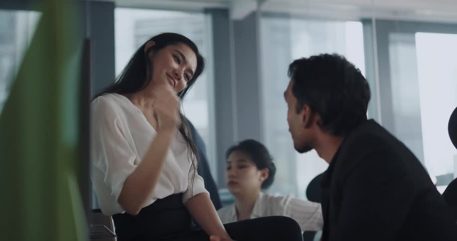 Woman sits on the desk of a coworker at the office with a coquettish and flirtatious attitude