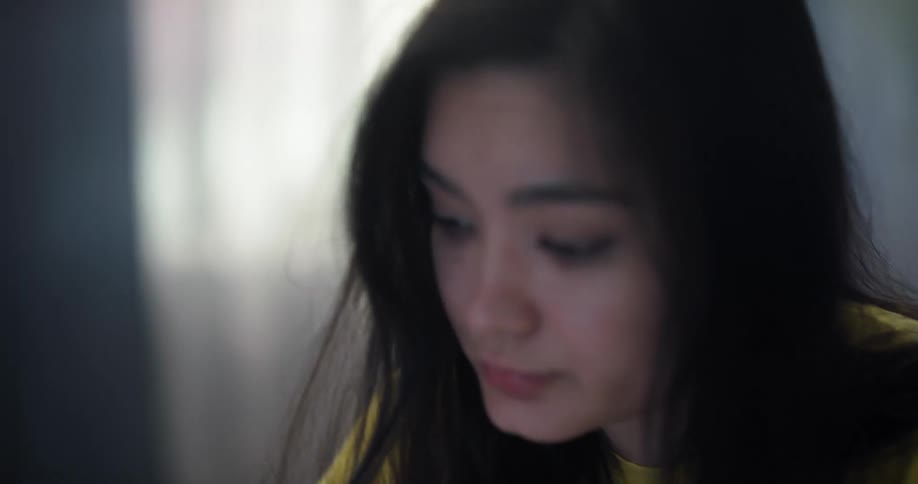 Tired and bored girl with straight hair and yellow t shirt sits at table