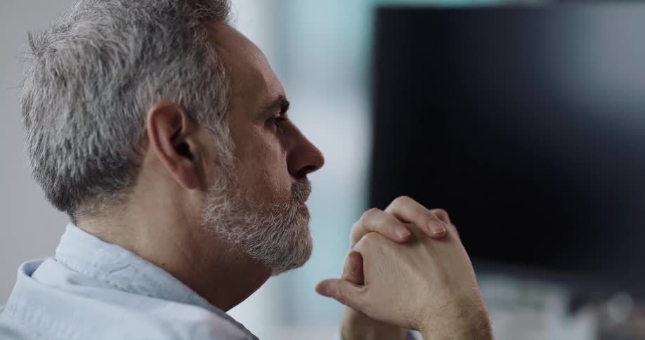 Man sits at desk with monitor listening and nodding to another