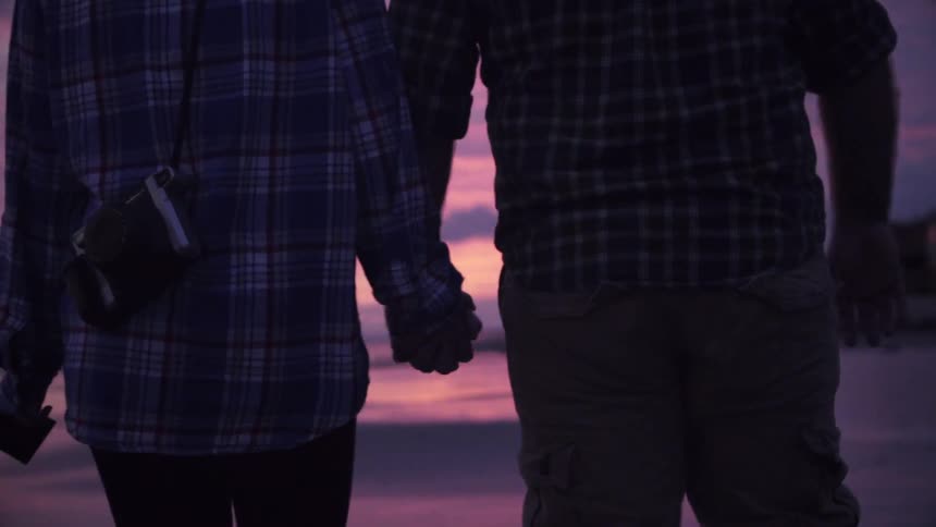 A couple walks down the beach at sunset