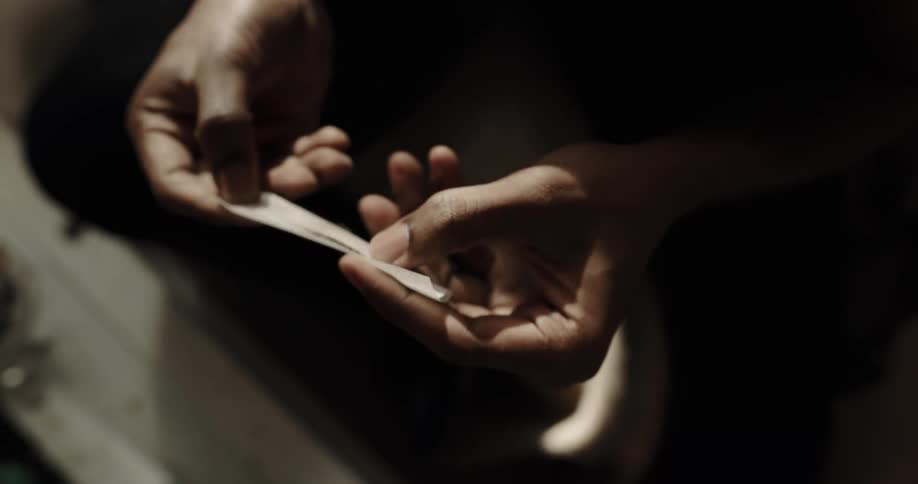 Young man sitting on the living room rolls a handmade cigarette