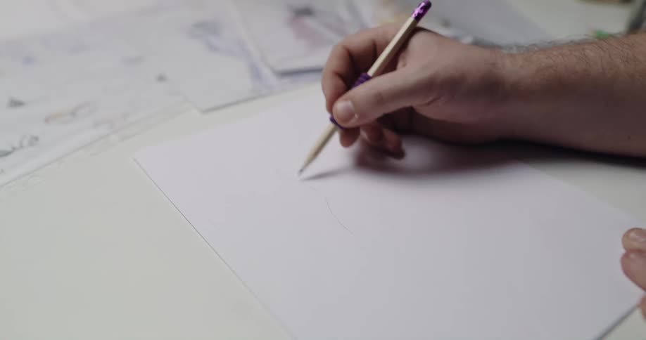 An artist is working on a sketch and other sketches lay across the table