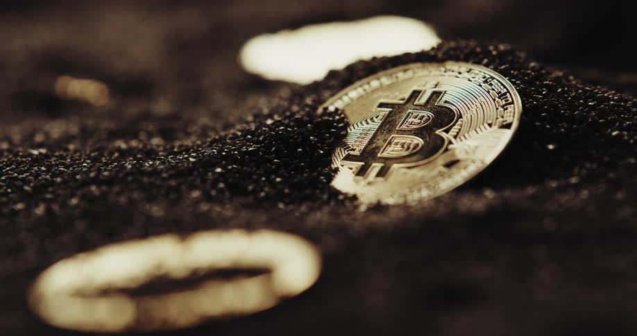 A few coins with the bitcoin cryptocurrency logo on them are partially buried in black powder