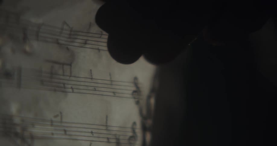 Silhouette of a hand writing musical notes on a music sheet using a pencil