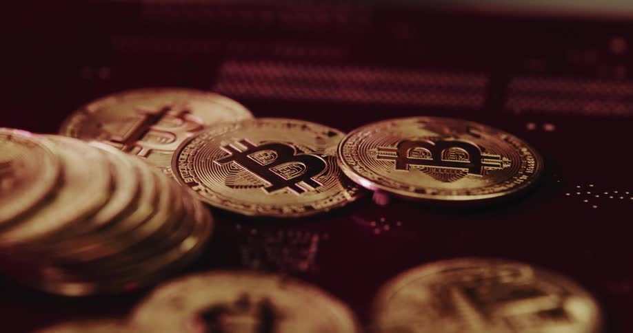 A number of reflective coins with the bitcoin logo on them are piled together
