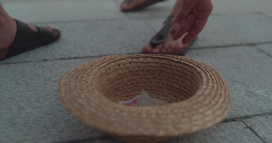 A man puts cash in a straw hat for a street performer