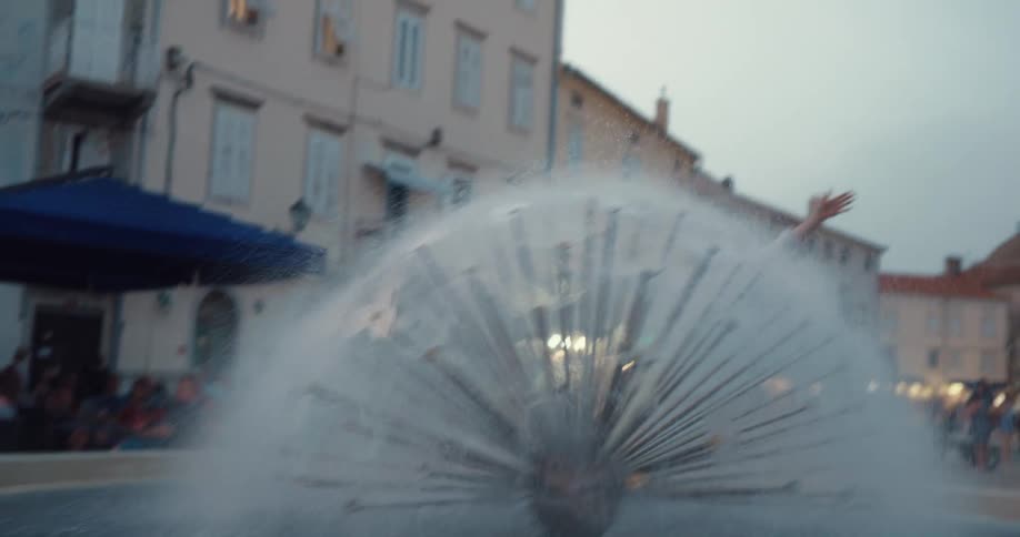 A woman walks atop the ledge of a water fountain before kissing a man waiting for her on one side
