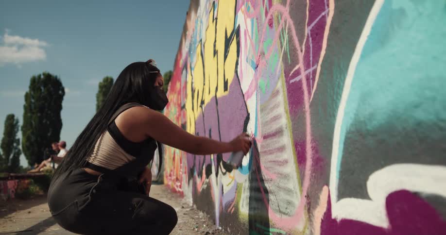 Woman wearing a face mask graffiting the wall of a public space using a spray bottle