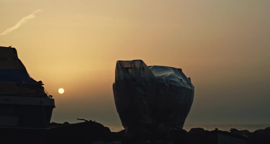 Boats over dry land covered with tarps in front of the sunset over the ocean