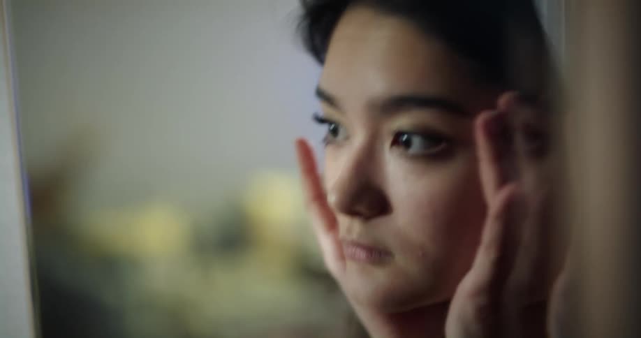 Young teenage woman rubs her eyelids and face with her fingers in front of a mirror at home