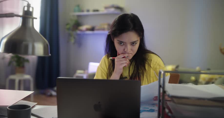 A young woman studies at a desk in a house during the day