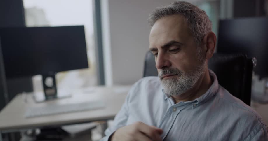 Businessman with shirt and beard sits in chair using tablet in the office