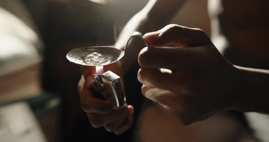 Person sits on couch cooking substance in spoon with a lighter