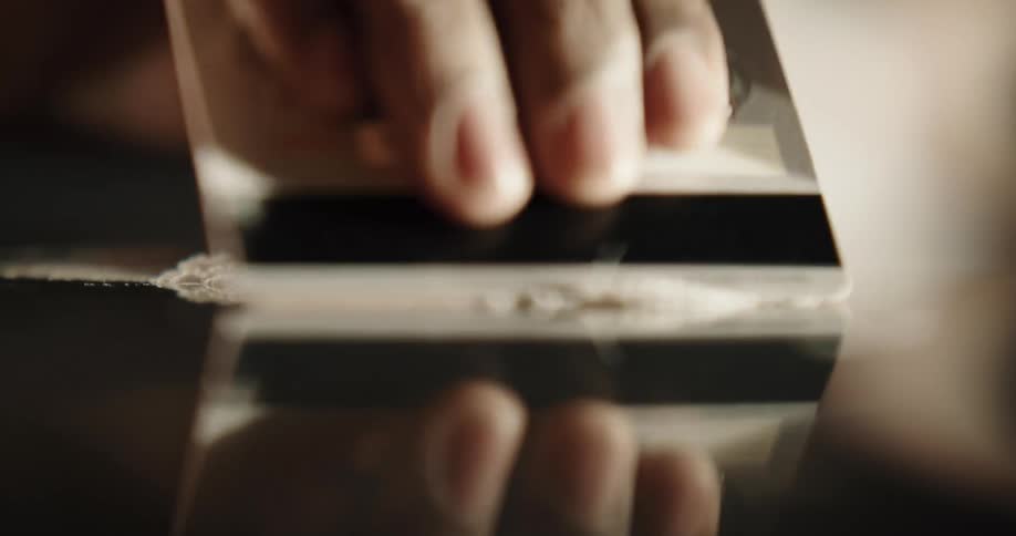A person uses a credit card to create a line of white powder on a reflective surface