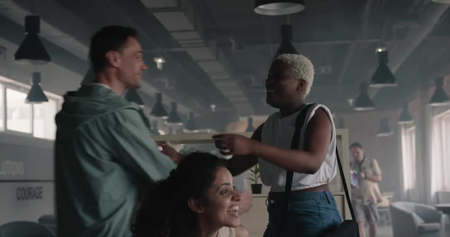 Woman with a purse walks towards a group of people and they each get up to greet and hug her