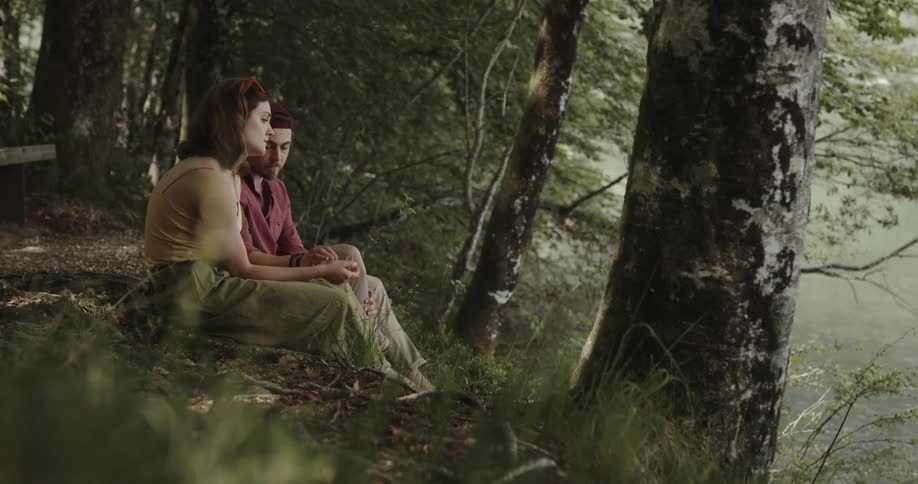 Young couple sitting on the forest ground near a lake talking to each other