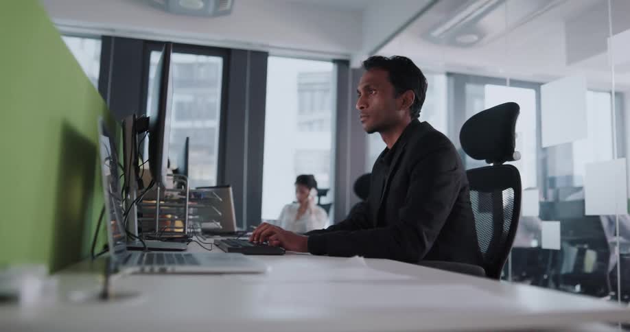 Man sits at a desk in an office and looks at a computer monitor as he types on a keyboard