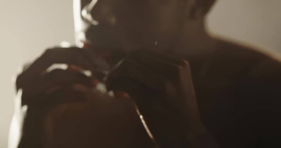 Shirtless black man rolling a joint and licking it to seal it