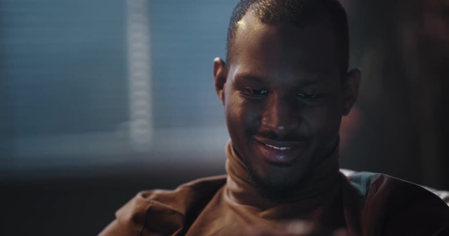 Man with brown turtleneck sweater uses smartphone smiling in living room at home