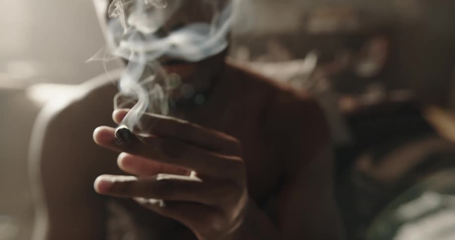 Man sits on living room couch lighting and smoking a marijuana roll
